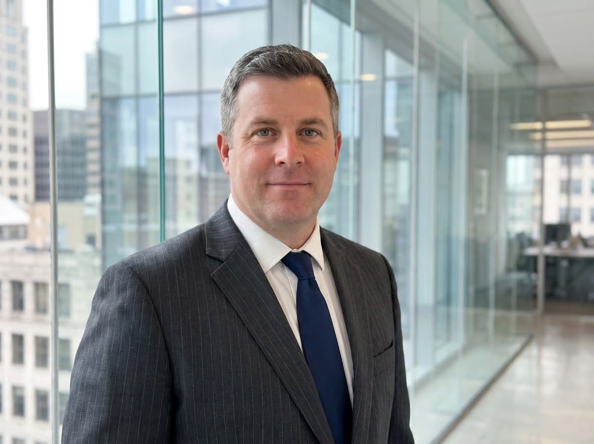 Senior partner Cabinet portrait — pinstripe charcoal suit, navy tie, contemporary glass-walled office